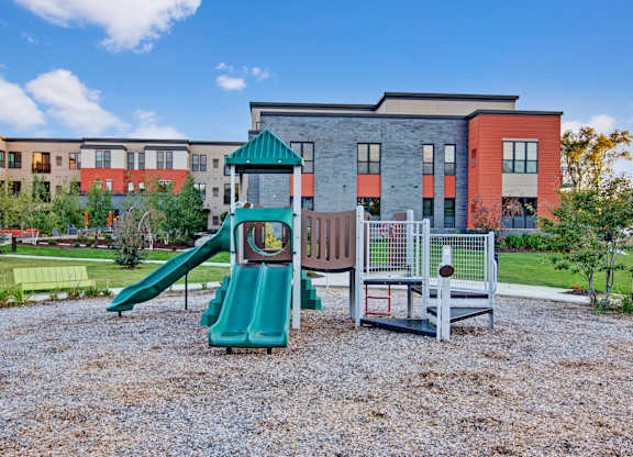 A playground with a green slide and a red and grey building in the background.
