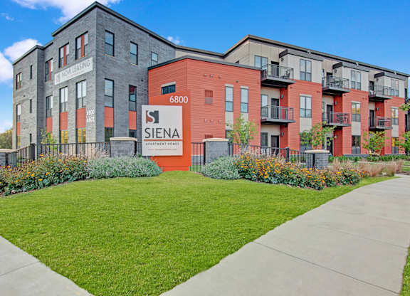 A Siena sign is in front of a building with a red and grey facade.