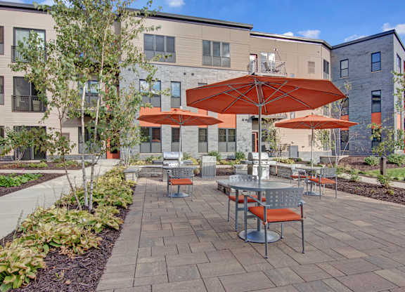 A patio with tables and chairs and umbrellas in front of apartment buildings.