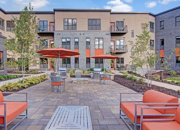 A courtyard with orange chairs and a table with a red umbrella.