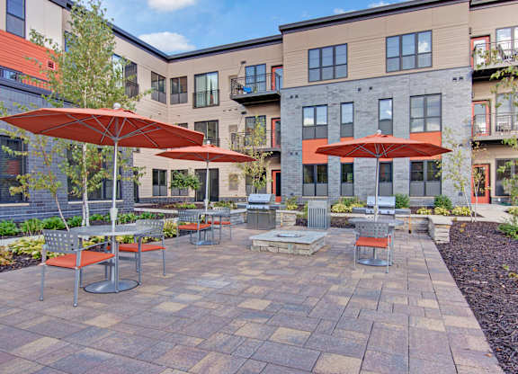 A patio with tables and chairs and umbrellas in front of apartment buildings.
