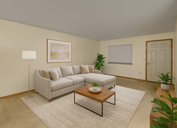 A bright, cozy living room here at Dakota featuring a light gray sectional sofa with neutral throw pillows, a wooden coffee table on a soft area rug, warm beige walls, indoor plants, simple wall art, and a floor lamp, creating a clean and inviting apartment living space.