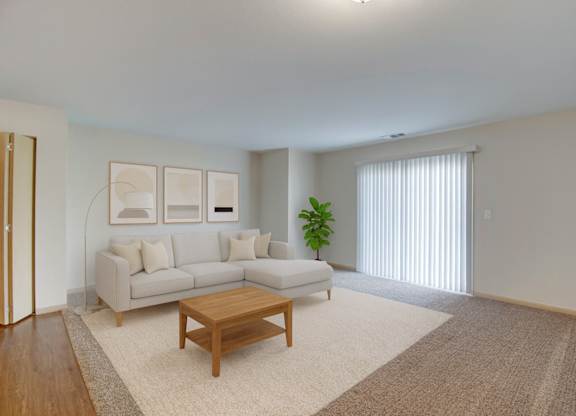 A bright living room here at Pheasant Ridge featuring a spacious open layout with a light gray sectional sofa, neutral throw pillows, a wooden coffee table, soft beige area rug, modern wall art, and a sliding glass door that fills the space with natural light and creates a warm, inviting atmosphere.