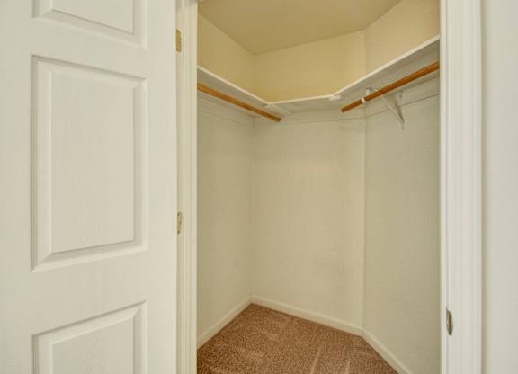 A spacious walk-in closet here at Phoenix Ridge featuring neutral carpet flooring, light-colored walls, double hanging rods with shelving for organized storage, and a wide doorway that highlights ample space for clothing, shoes, and seasonal items.