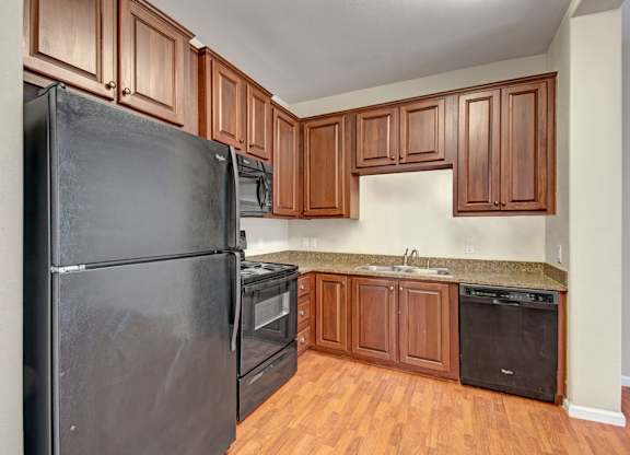 A bright kitchen here at Prairie Vista showcasing rich wood cabinetry, black appliances, granite-style countertops, wood-look flooring, and a functional L-shaped layout that offers ample storage and counter space for everyday cooking and entertaining.