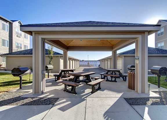 A covered picnic area with tables and benches is surrounded by apartment buildings.