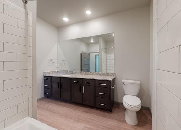 A white toilet sits in a bathroom with a large mirror and a counter with a sink.