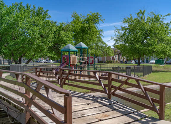 A wooden bridge leads to a playground in a park.