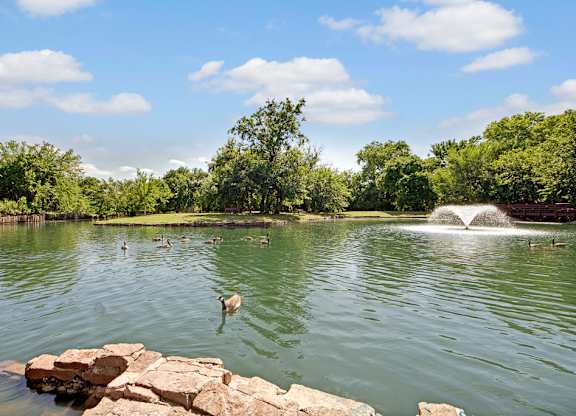 A fountain in the middle of a lake with a duck jumping into the water.