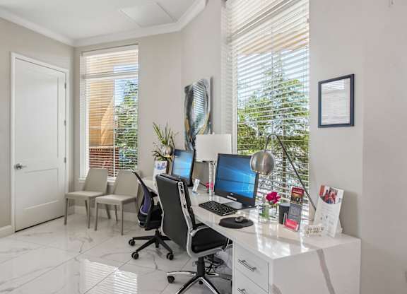 A white desk with a computer and a chair in front of a window with blinds.