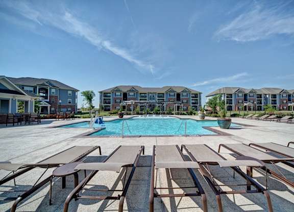 A swimming pool surrounded by sun loungers in front of apartment buildings.