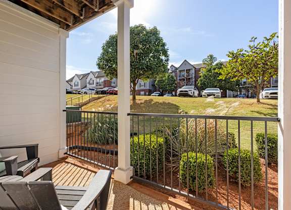 A private patio here at Lincoln at Central Park featuring black outdoor seating, a light cushion, black metal railing, landscaped greenery, and open neighborhood views in bright natural daylight.