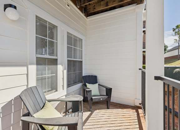 A patio space here at Lincoln at Central Park featuring black outdoor chairs with light green cushions, white siding, large windows, black railing, and bright natural sunlight creating a clean, welcoming outdoor sitting area.