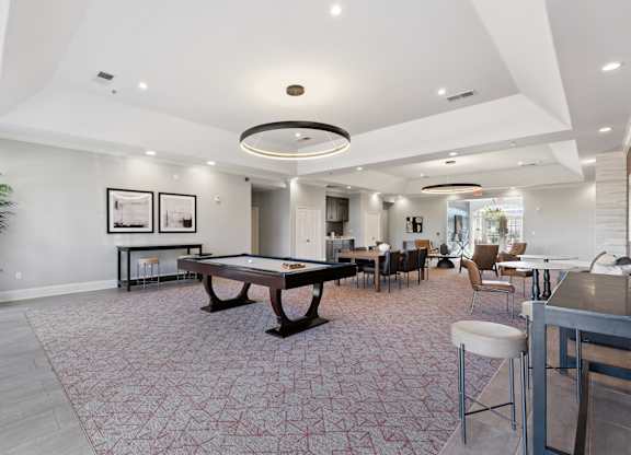 A spacious resident lounge here at Lincoln at Central Park with plush carpet flooring, a pool table, dining table seating, and modern circular ceiling lighting. A neutral color palette and comfortable seating areas create a welcoming, upscale gathering space.