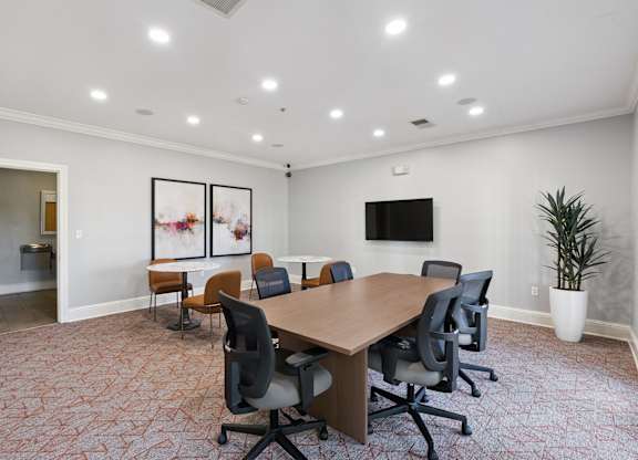 A private conference room here at Lincoln at Central Park with a large wood meeting table, rolling office chairs, and bright recessed lighting. A wall-mounted TV, abstract artwork, and modern seating create a professional, comfortable workspace.