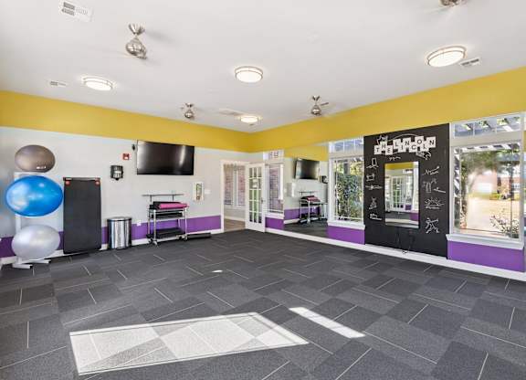 A spacious fitness studio here at Lincoln at Central Park with large windows, mirrored walls, and bright accent colors. A mounted TV, exercise balls, and workout mats create a versatile, motivating space for fitness classes or personal workouts.