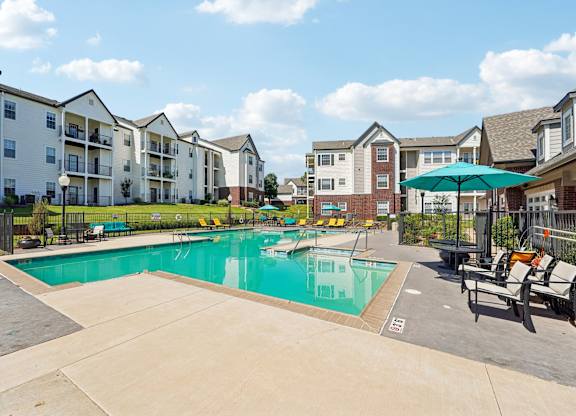 A swimming pool surrounded by apartment buildings and lounge chairs.