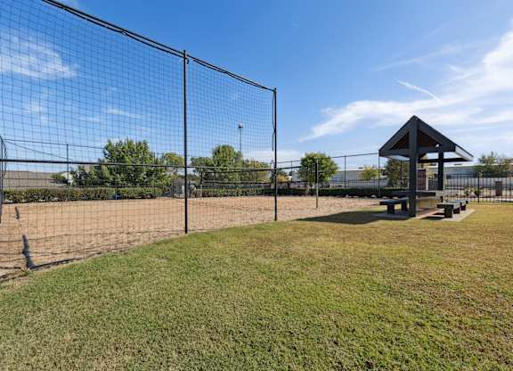 A black fence surrounds a green field with a pavilion in the background.