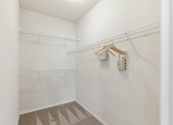 A walk-in closet here at Quail Landing with white wire shelving on two walls, neutral carpet flooring, bright white walls, and a clean, empty layout offering simple storage space.