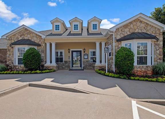 A leasing office exterior here at Quail Landing with a stone façade, columned entry, manicured landscaping, and a welcoming front entrance under a bright blue sky.