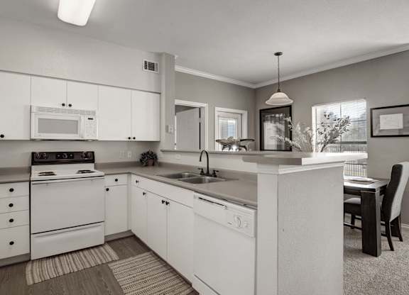 A spacious kitchen here at Stoneleigh on May with white cabinets, light countertops, and matching white appliances. A breakfast bar opens to the dining area, while bright lighting and neutral finishes create a clean, welcoming feel.