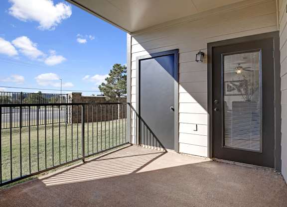 A private patio here at Stoneleigh on May with a covered concrete floor, metal railing, and exterior storage closet. An outdoor door with blinds connects to the living space, offering a bright, open, and relaxing outdoor retreat.