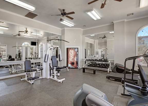 A well-equipped fitness center here at Stoneleigh on May with cardio machines, weight equipment, mirrored walls, and bright lighting. Ceiling fans and open space create an energizing, comfortable workout environment.