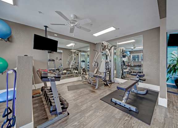 A spacious gym with a variety of equipment and a television mounted on the wall.