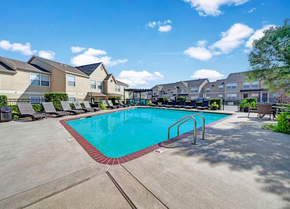 A swimming pool surrounded by a concrete patio and a row of houses.
