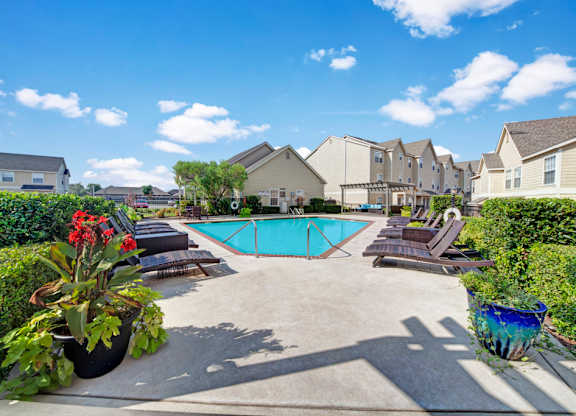 A pool surrounded by lounge chairs and plants.