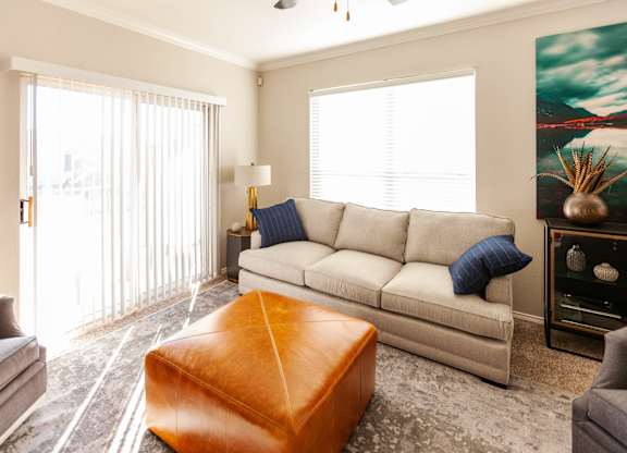 A living room with a grey couch, a brown ottoman, and a painting on the wall.