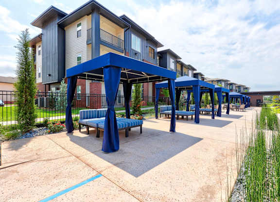 An outdoor lounge here at The Encore with blue cabanas, cushioned seating, and landscaped walkways. The bright, open space feels relaxed and inviting, with modern buildings and greenery creating a resort-style setting.
