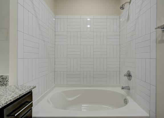 A white tiled bathroom with a white bathtub and a marble countertop.