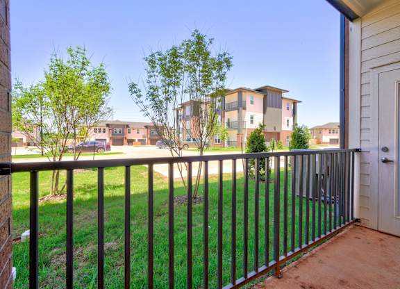 A balcony with a black railing overlooks a grassy area and apartment buildings.