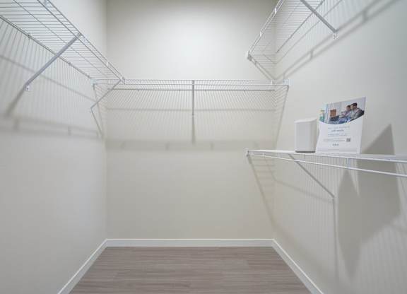 A walk-in closet here at The Encore with white wire shelving on three walls, soft neutral walls, and wood-style flooring. The empty space feels bright, clean, and practical for organized storage.