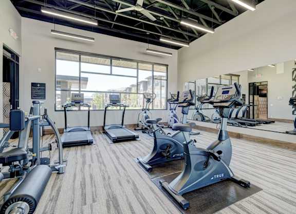 A fitness center here at The Encore with cardio machines, mirrored walls, and large windows. The open layout feels bright and modern, with high ceilings and natural light creating an energizing workout space.