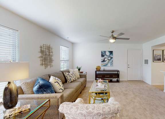 A living room with a couch, coffee table, and a fan.