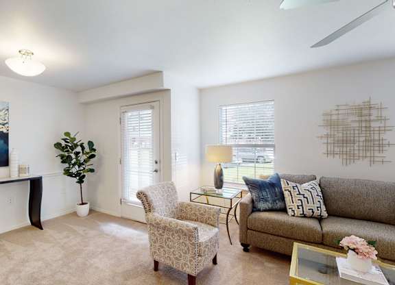 A living room with a grey couch, a yellow bowl on a black table, a painting on the wall, a plant, a chair, and a coffee table.