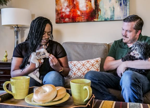 A man and woman sitting on a couch with two dogs at Confluence at Harvest Hills