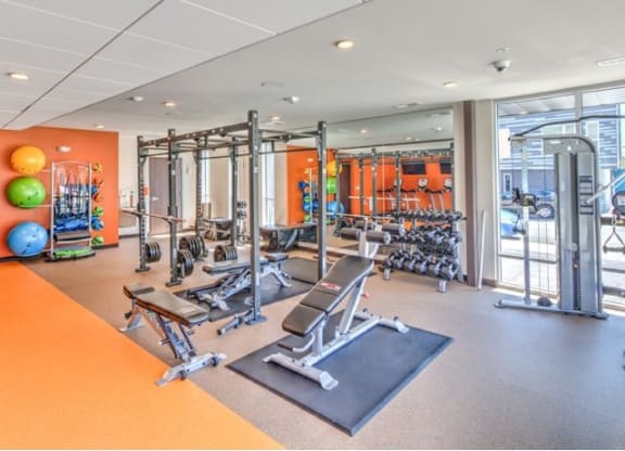 Modern gym with weightlifting equipment, exercise balls, and mirrors. Bright and spacious with warm-toned walls, creating an inviting atmosphere at Stitchweld Apartments.