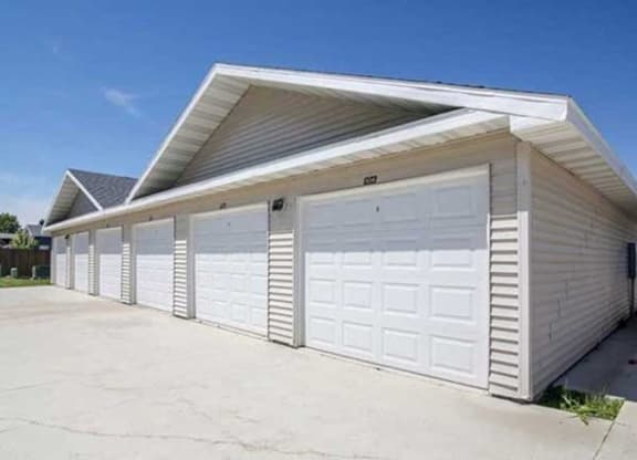 A row of beige garages here at Phoenix Ridge Apartment Homes with white doors under a clear blue sky. The garages are aligned on a smooth concrete surface, conveying tidiness and order.