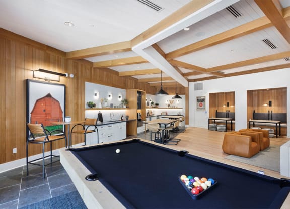 Modern lounge here at Reflect at Dobson Ranch Apartments with a pool table, bar stools, a kitchenette, and cozy seating. The wooden walls and beams create a warm, inviting atmosphere.
