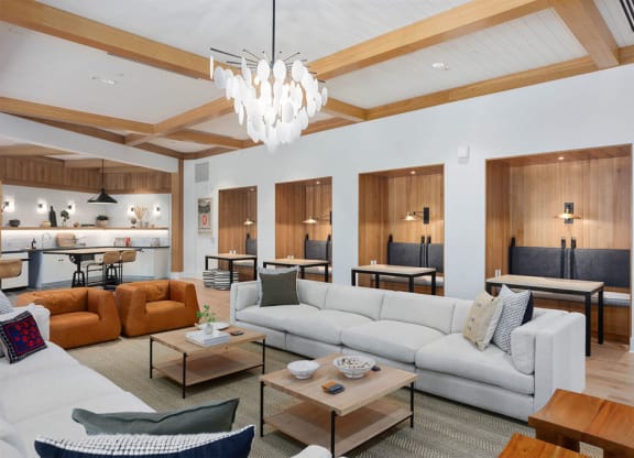 Modern resident lounge here at Reflect at Dobson Ranch Apartments with cozy seating, light wood accents, and a sleek chandelier. Features leather chairs, white sectional, and wood dining booths, creating a warm, inviting atmosphere.