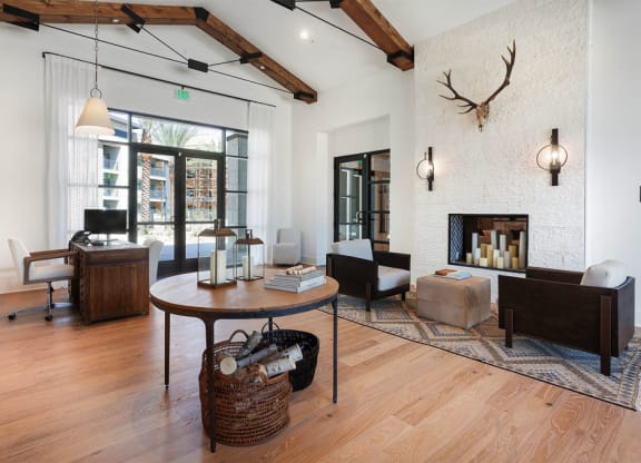 Modern living room here at Reflect at Dobson Ranch Apartments with wood beams, a large round table, baskets underneath, and armchairs by a white stone fireplace adorned with deer antlers.