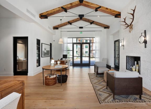 Modern living room here at Reflect at Dobson Ranch Apartments with high wooden beam ceiling, antler decor, and cozy fireplace. Natural light through glass doors creates a warm, inviting atmosphere.