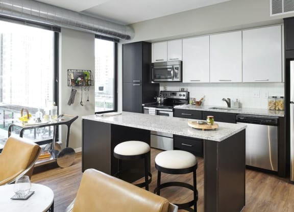 Modern kitchen here at 4Marq Apartment Homes with black and white cabinetry, stainless steel appliances, and a granite island with two stools. Bright, minimalistic, urban feel.
