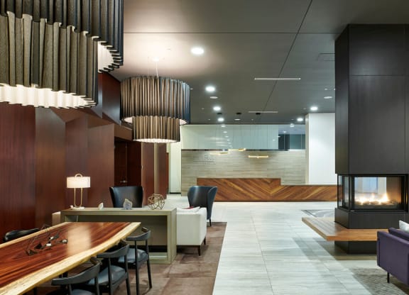 Spacious modern lobby here at here at 4Marq Apartments with wood accents, large lampshades, and a cozy fireplace. Features sleek furniture, warm lighting, and a welcoming ambiance.