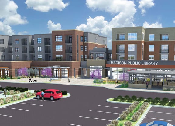 Modern library and apartment complex with red brick and gray accents under a bright blue sky. A red car and pedestrians are in the foreground of Royster Apartment Homes.