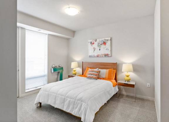 A cozy bedroom here at Blue and Lime Apartments with a double bed featuring orange and white bedding. Yellow lamps sit on both wooden nightstands. A colorful world map hangs above.