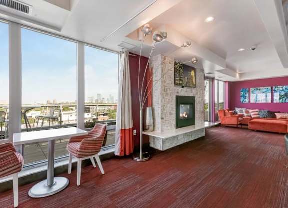 Spacious modern lounge here at Blue and Lime Apartments with red carpet, a cozy fireplace, and large windows offering a cityscape view. Features red chairs and a sectional sofa.